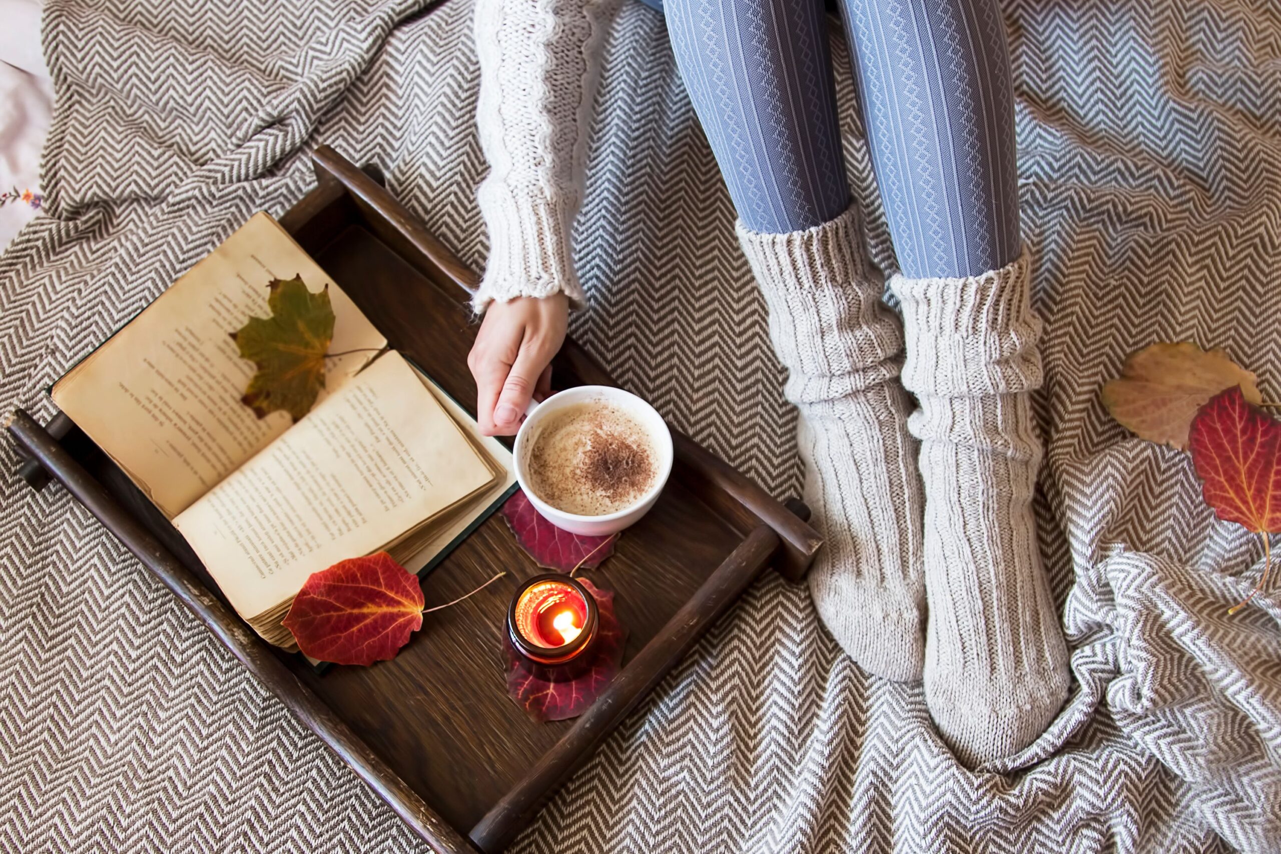 Image of someone with plush warm socks on, reading a book with some cocoa